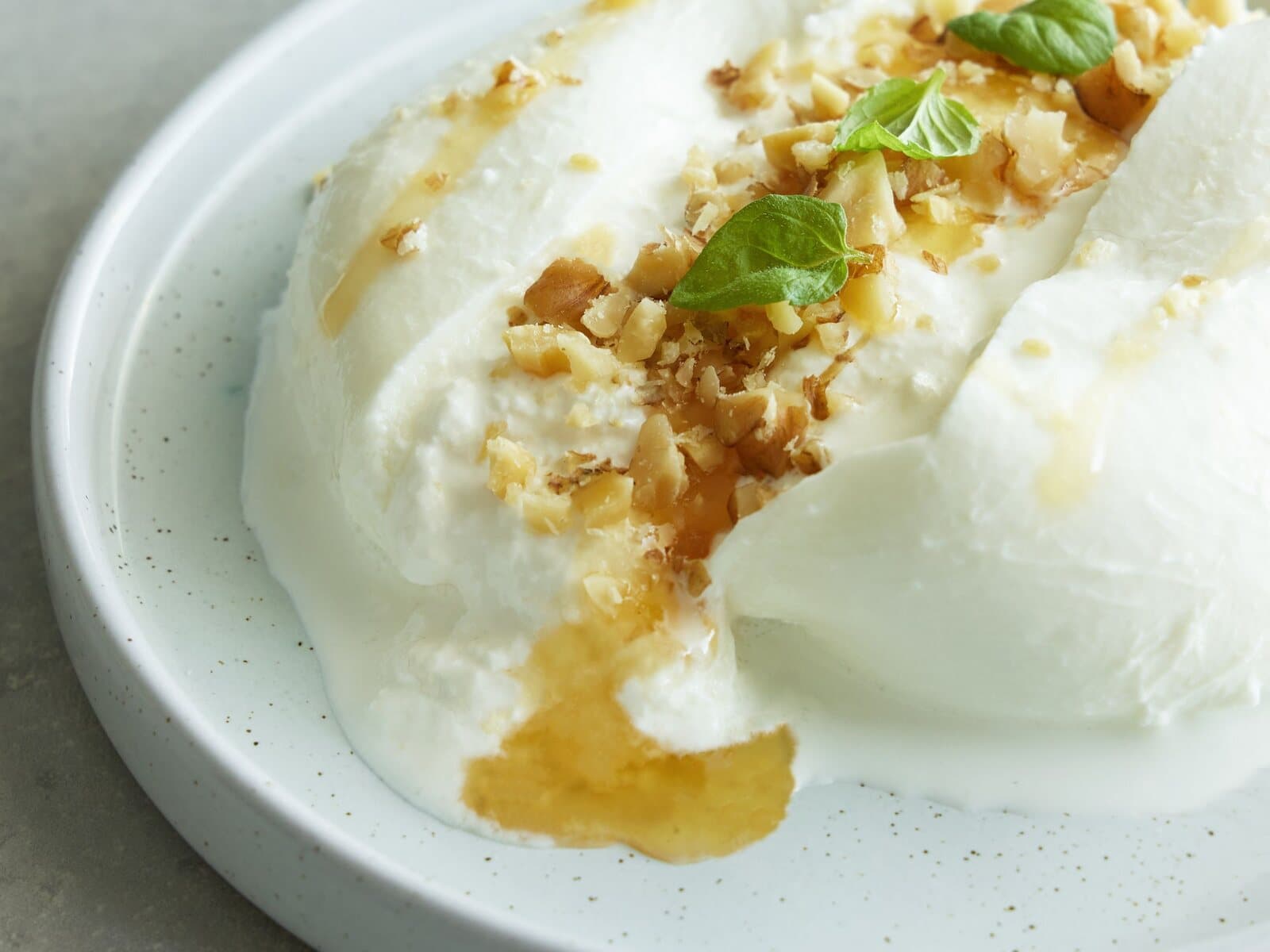 Creamy burrata drizzled with honey and topped with chopped nuts on a white plate.