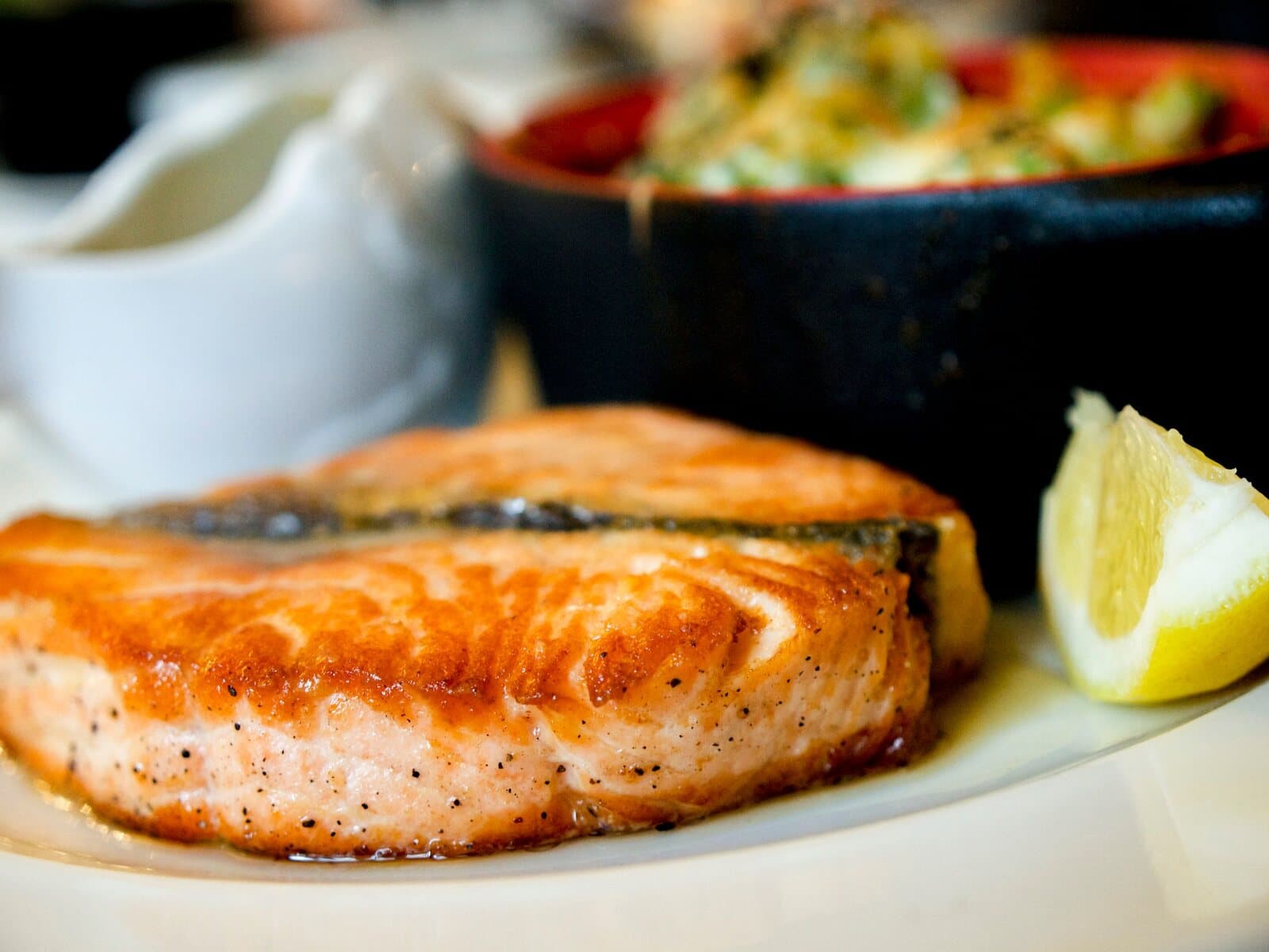 Seared salmon steak with a lemon wedge on a white plate.