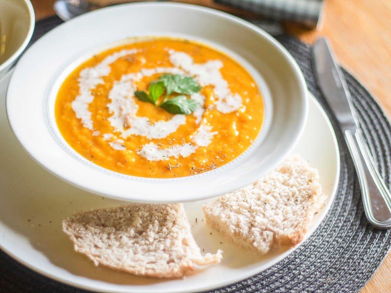 A white bowl of butternut squash bisque with a swirl of cream and fresh parsley.